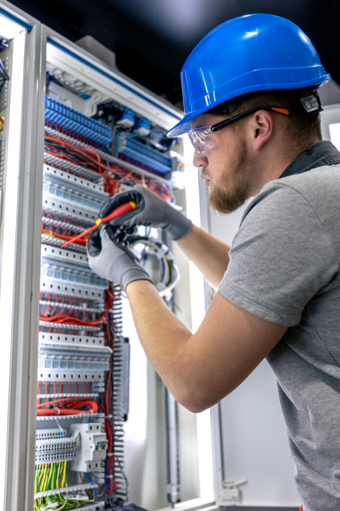 Male electrician in uniform working in a switchboard. Electricity.